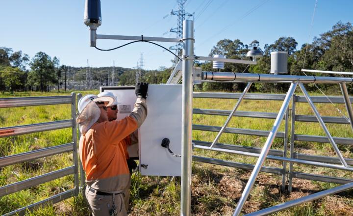 men in PPE in field with weather sensor 